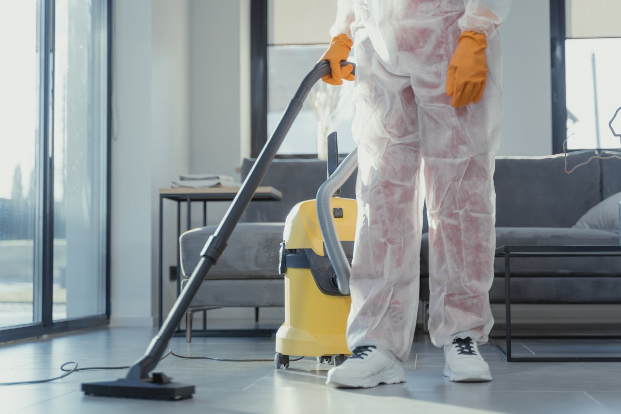 about-01 A cleaner in protective coveralls and gloves vacuuming a modern living room.